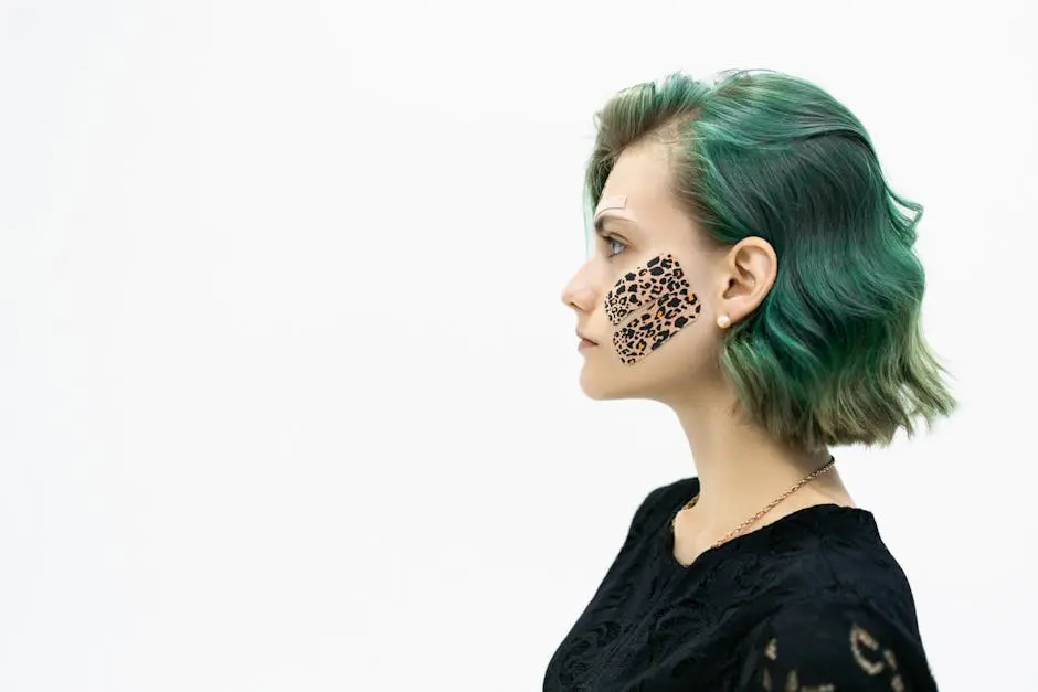 Profile portrait of a young woman with green hair and kinesio tape on her cheek on a white background.